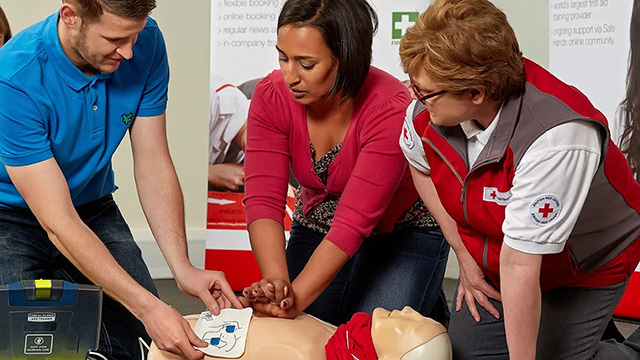 Image of two adults and a British Red Cross trainer administering First Aid to a dummy