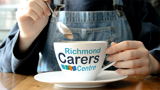A woman stirring a coffee cup with the Richmond Carers logo on it