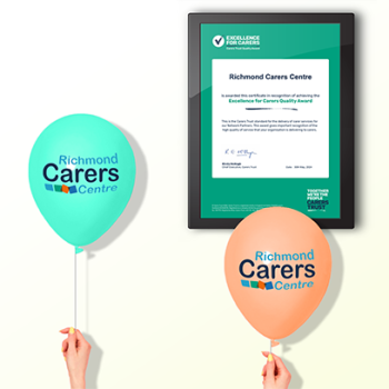 Image shows a framed certificate of the Excellence for Carers award with Richmond Carers Centre branded balloons